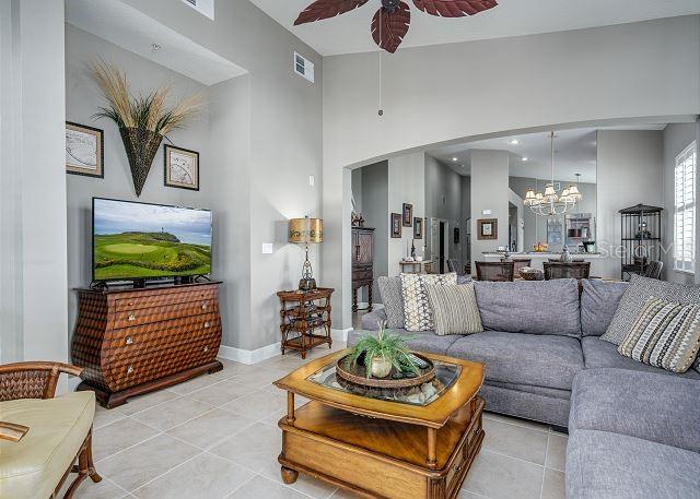 living room with a towering ceiling, light tile patterned floors, and ceiling fan with notable chandelier