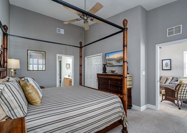 bedroom with light carpet, a high ceiling, ensuite bath, ceiling fan, and a closet