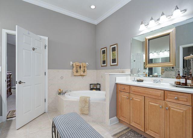 bathroom with tile patterned flooring, vanity, crown molding, and tiled bath