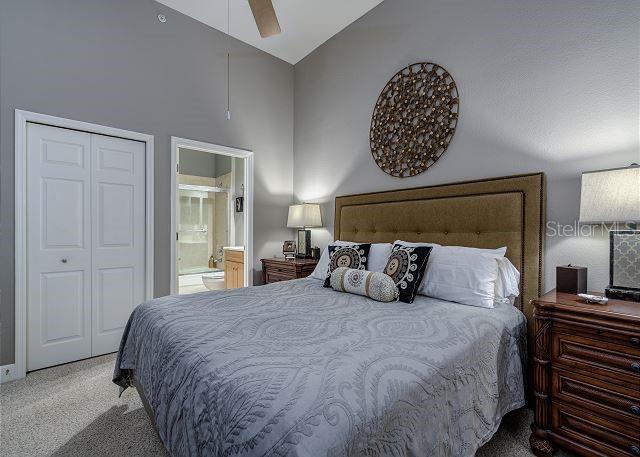 bedroom featuring carpet, ensuite bathroom, vaulted ceiling, ceiling fan, and a closet