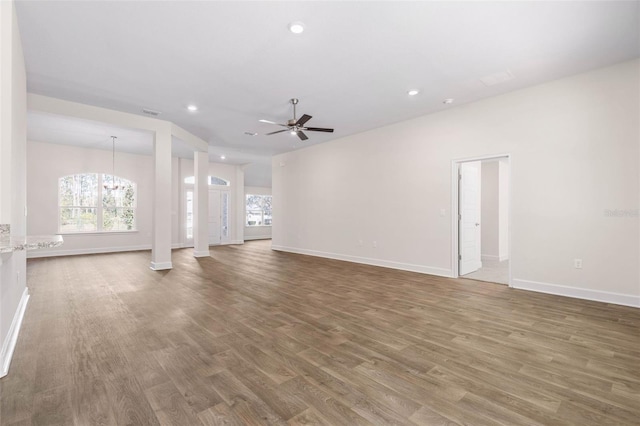 unfurnished living room with ceiling fan with notable chandelier and wood-type flooring