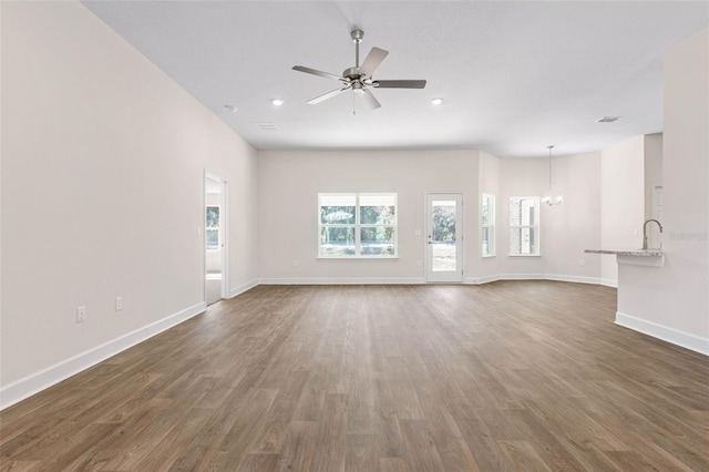 unfurnished living room featuring ceiling fan with notable chandelier and dark hardwood / wood-style flooring