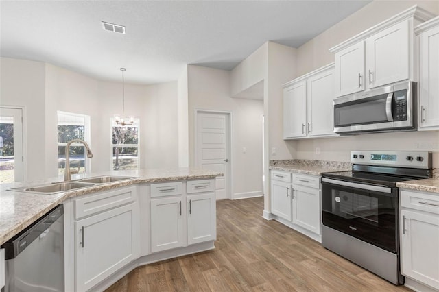 kitchen featuring white cabinets, appliances with stainless steel finishes, decorative light fixtures, sink, and light wood-type flooring