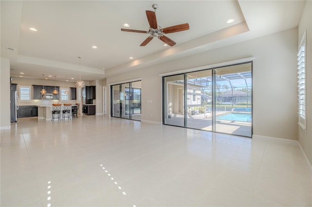 unfurnished living room with ceiling fan, light tile patterned flooring, and a raised ceiling