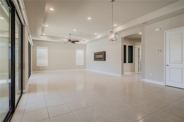 tiled spare room with a raised ceiling and ceiling fan with notable chandelier