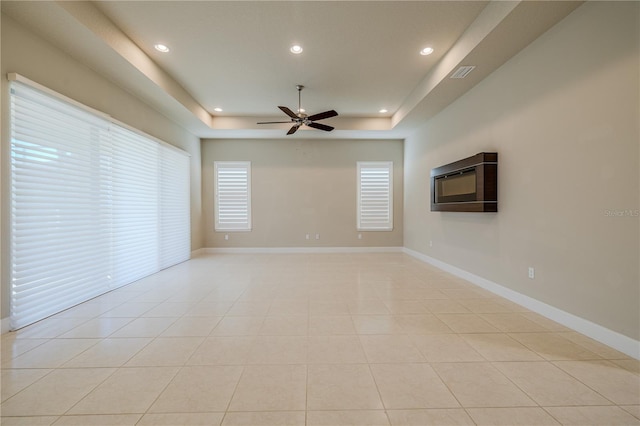 tiled spare room with ceiling fan and a tray ceiling