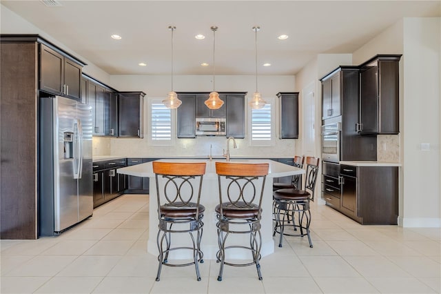 kitchen featuring pendant lighting, light tile patterned floors, appliances with stainless steel finishes, a kitchen island, and dark brown cabinetry