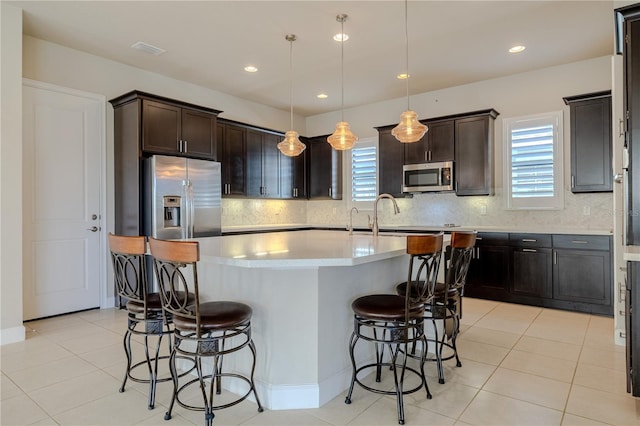 kitchen with dark brown cabinetry, stainless steel appliances, pendant lighting, a breakfast bar area, and a kitchen island