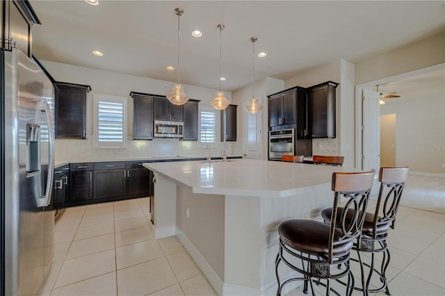 kitchen featuring a kitchen island with sink, decorative light fixtures, decorative backsplash, light tile patterned flooring, and appliances with stainless steel finishes