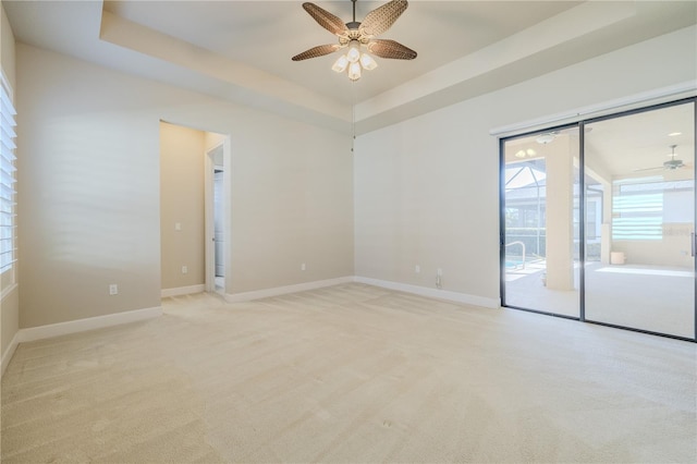 carpeted spare room featuring a tray ceiling and ceiling fan