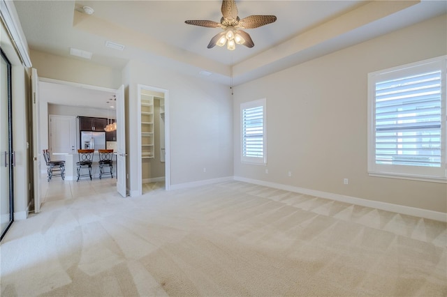 carpeted empty room with a tray ceiling and ceiling fan