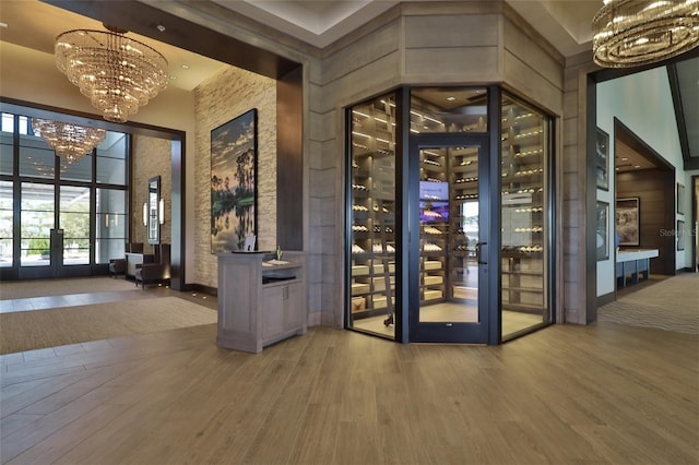 wine room featuring hardwood / wood-style flooring, an inviting chandelier, a towering ceiling, and french doors