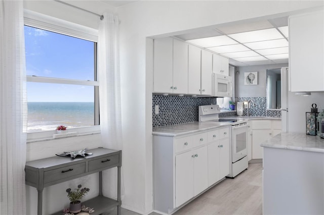 kitchen featuring white cabinets, a water view, white appliances, and a wealth of natural light