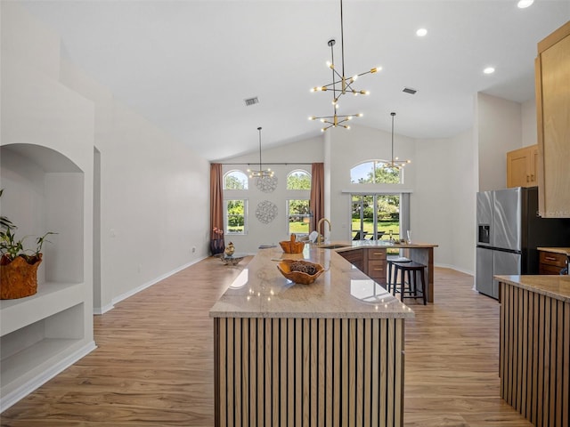 kitchen featuring sink, stainless steel fridge with ice dispenser, pendant lighting, light hardwood / wood-style floors, and a kitchen island with sink