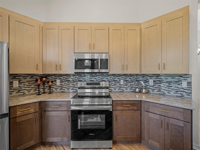 kitchen with tasteful backsplash, light stone countertops, appliances with stainless steel finishes, and light hardwood / wood-style flooring