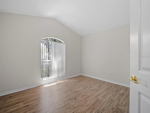 spare room with hardwood / wood-style floors and vaulted ceiling