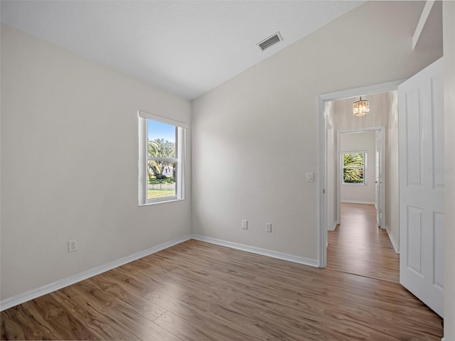 spare room featuring a chandelier, plenty of natural light, hardwood / wood-style floors, and vaulted ceiling