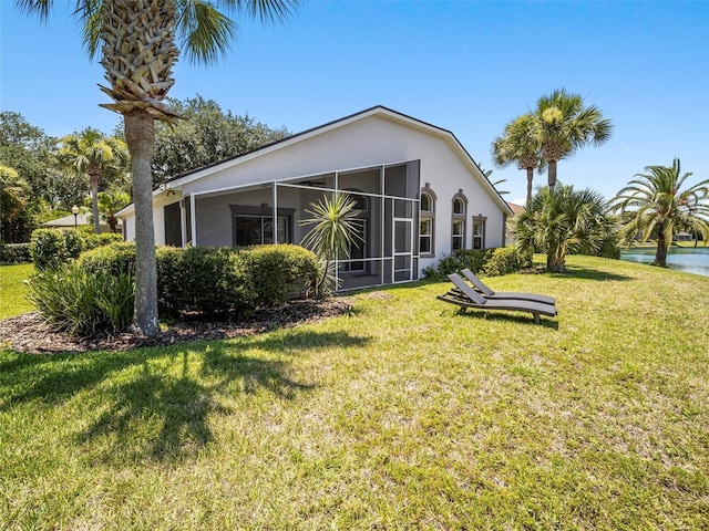 back of house with a sunroom, a water view, and a lawn