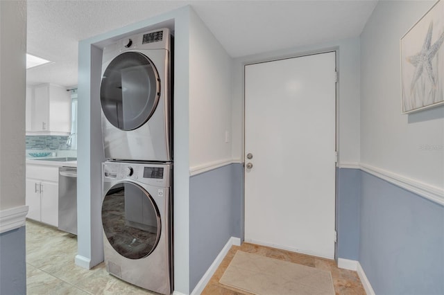 clothes washing area featuring sink, stacked washing maching and dryer, and a textured ceiling