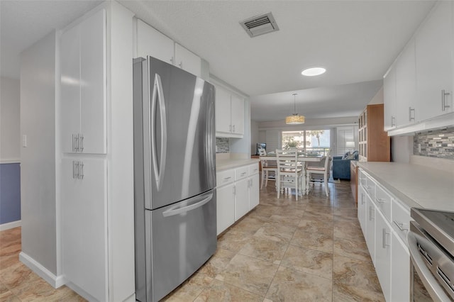 kitchen with stainless steel fridge, white cabinetry, and hanging light fixtures