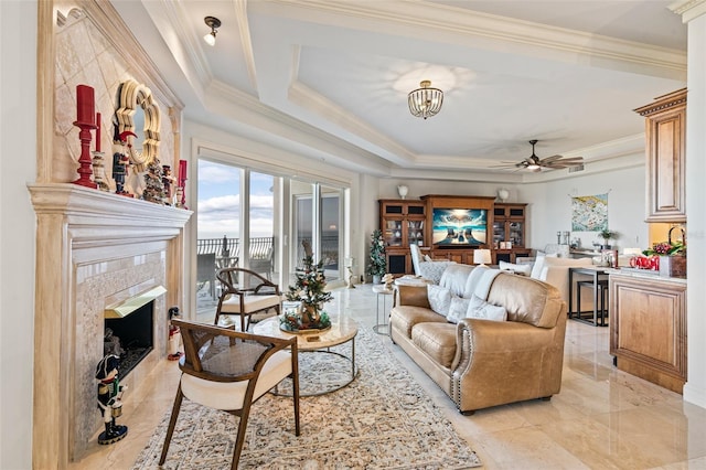 living room featuring ceiling fan with notable chandelier, crown molding, a fireplace, and a tray ceiling