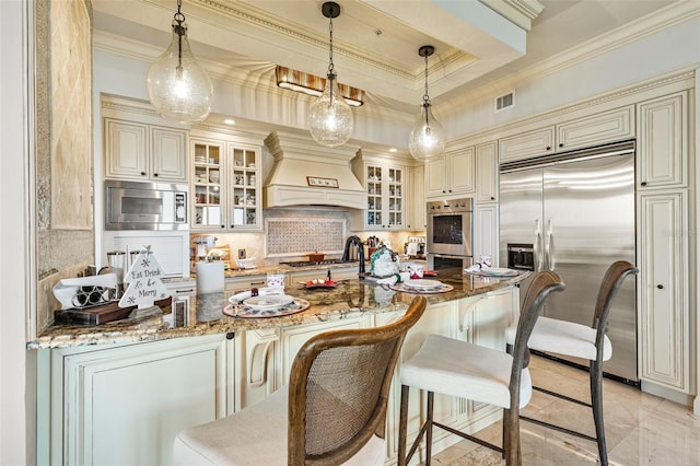 kitchen with dark stone countertops, crown molding, built in appliances, and custom range hood