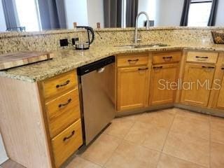 kitchen with a sink, light stone counters, stainless steel dishwasher, and light tile patterned floors