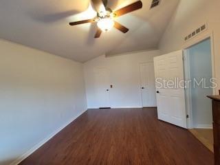 empty room with vaulted ceiling, wood finished floors, visible vents, and ceiling fan