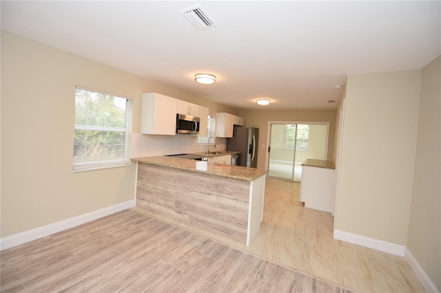 kitchen with kitchen peninsula, stainless steel appliances, light stone countertops, sink, and white cabinets