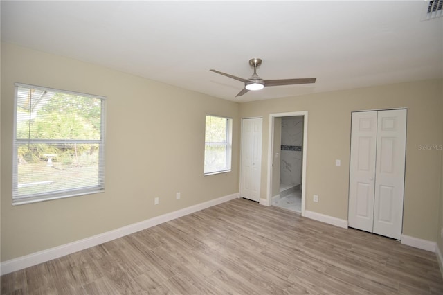 unfurnished bedroom featuring ceiling fan, light hardwood / wood-style flooring, multiple windows, and ensuite bath