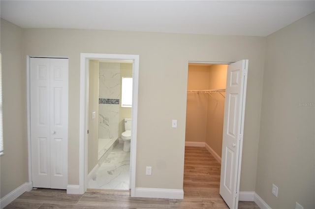 unfurnished bedroom with ensuite bathroom, light wood-type flooring, a closet, and a spacious closet