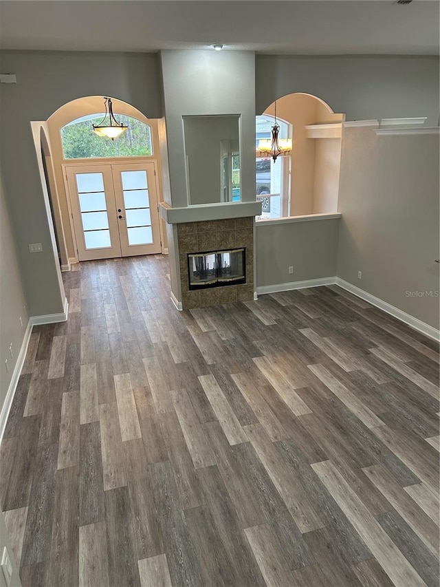 unfurnished living room with a tile fireplace, french doors, dark wood-type flooring, and a notable chandelier