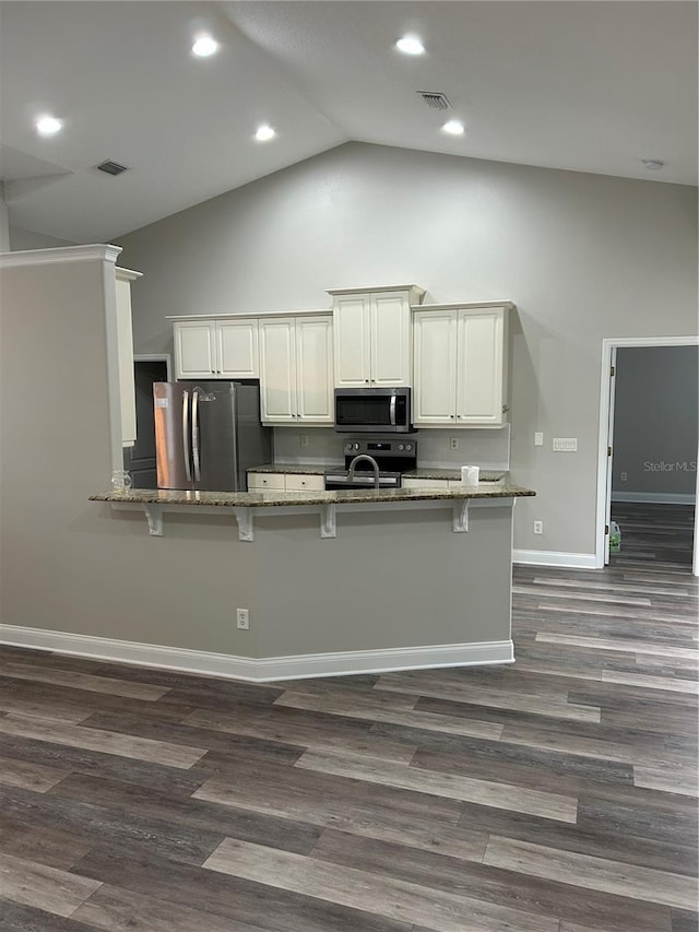 kitchen with kitchen peninsula, a breakfast bar, stainless steel appliances, dark wood-type flooring, and stone countertops