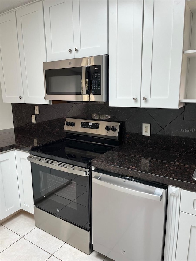 kitchen with white cabinets, dark stone countertops, light tile patterned floors, appliances with stainless steel finishes, and tasteful backsplash