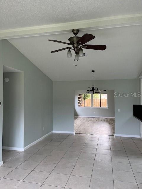 empty room with a textured ceiling, vaulted ceiling with beams, light tile patterned floors, and ceiling fan with notable chandelier