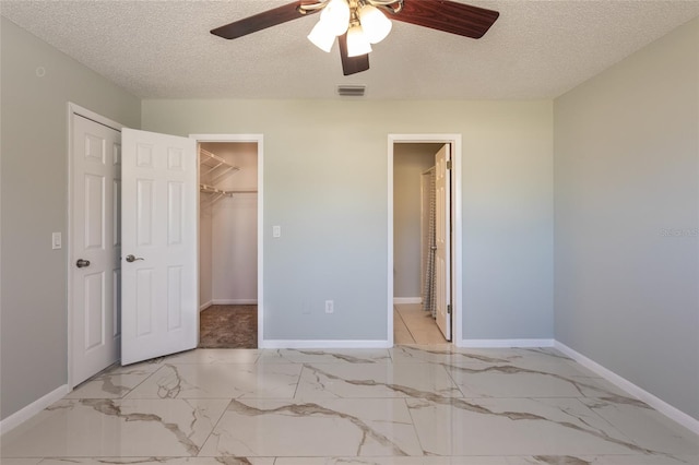 unfurnished bedroom with ceiling fan, a spacious closet, a textured ceiling, and a closet