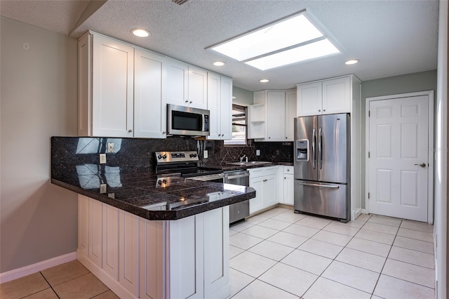 kitchen with white cabinets, decorative backsplash, light tile patterned floors, kitchen peninsula, and stainless steel appliances