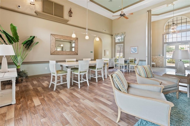 interior space with a towering ceiling, wood-type flooring, a tray ceiling, and ceiling fan with notable chandelier