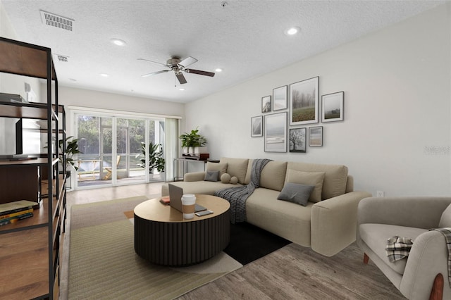 living room with wood-type flooring, ceiling fan, and a textured ceiling