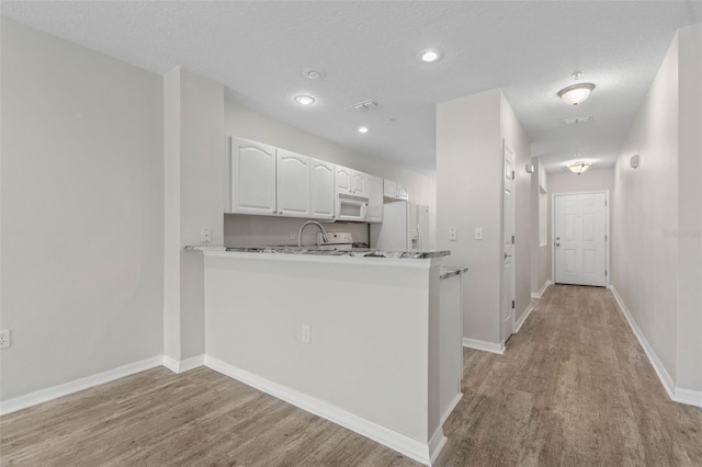 kitchen with a textured ceiling, light wood-type flooring, kitchen peninsula, white appliances, and white cabinets