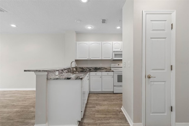 kitchen featuring sink, kitchen peninsula, white appliances, dark stone counters, and white cabinets