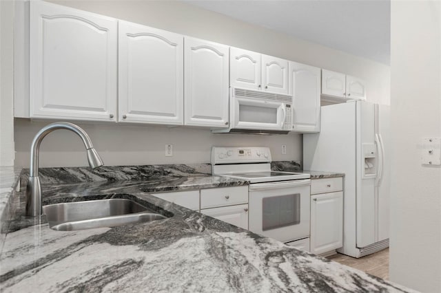 kitchen featuring sink, white cabinetry, light wood-type flooring, dark stone countertops, and white appliances