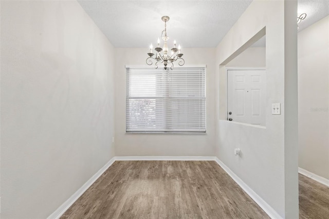 unfurnished dining area with wood-type flooring, a textured ceiling, and a chandelier