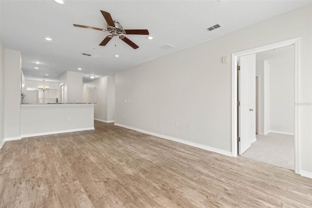 unfurnished living room with ceiling fan with notable chandelier and light wood-type flooring