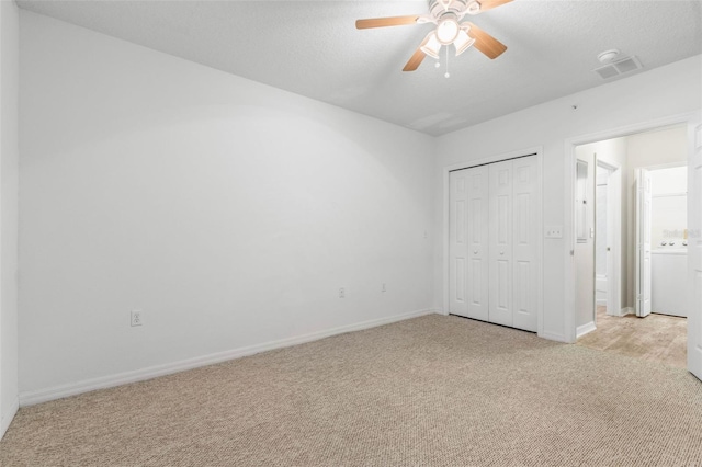 unfurnished bedroom featuring light colored carpet, a textured ceiling, a closet, ceiling fan, and washer / clothes dryer