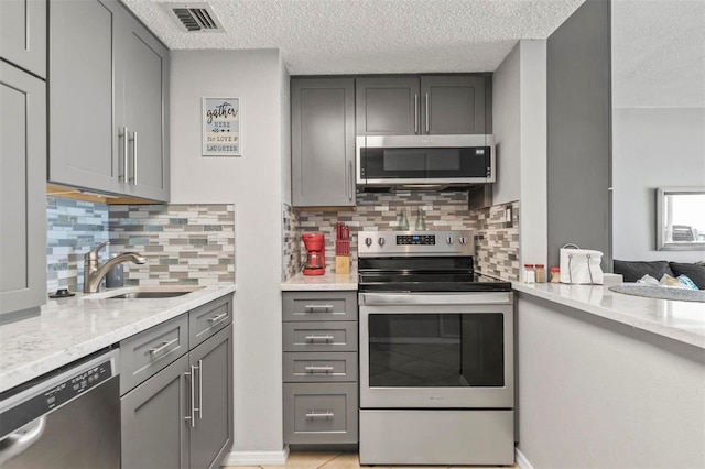 kitchen featuring backsplash, gray cabinetry, light stone countertops, and appliances with stainless steel finishes