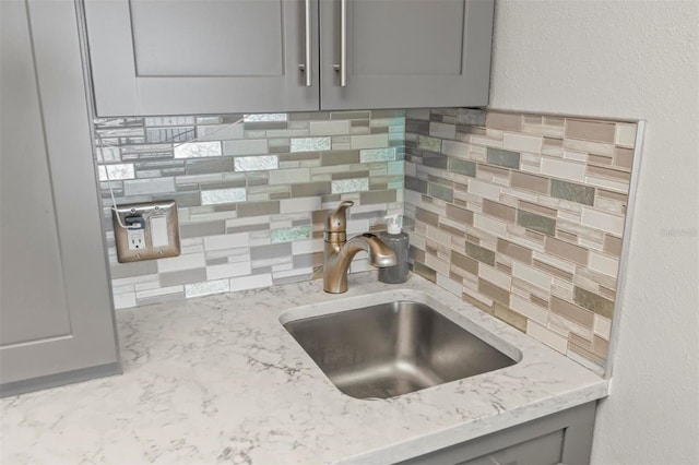 room details featuring gray cabinetry, sink, light stone countertops, and backsplash