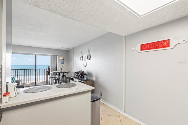 kitchen featuring a textured ceiling, a water view, light tile patterned floors, and hanging light fixtures