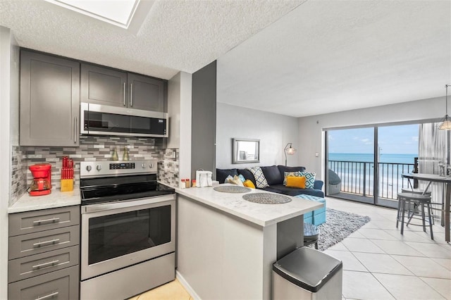 kitchen with stainless steel appliances, kitchen peninsula, a textured ceiling, decorative backsplash, and a water view