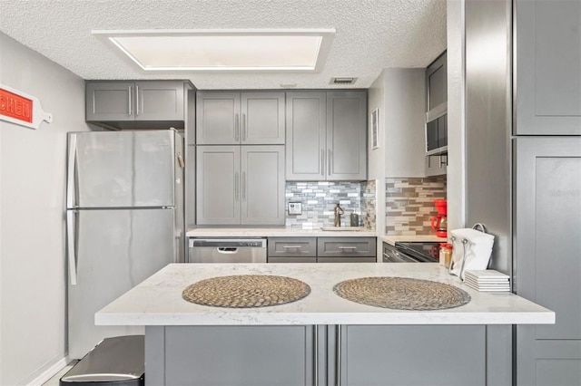 kitchen featuring backsplash, kitchen peninsula, gray cabinets, and appliances with stainless steel finishes